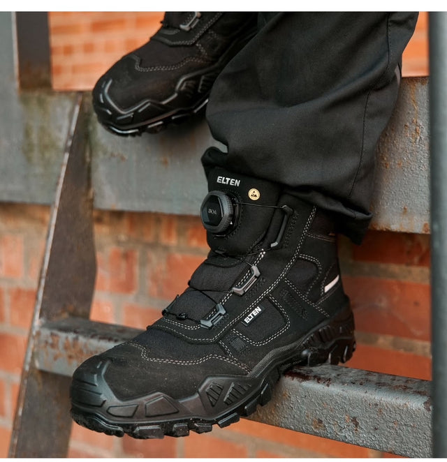 A person wearing black work boots Mike with BOA dial closure system, on a ladder to show the ladder grip sole of the boot.
