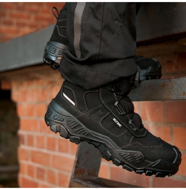 A person wearing black work boots Mike with BOA dial closure system, on a ladder to show the ladder grip sole of the boot.